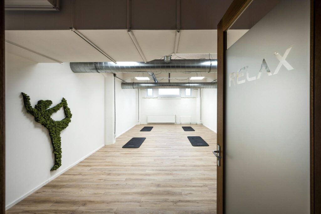 Minimalist yoga studio on Van Diemenstraat with black mats, wooden floor, and a moss wall art figure.